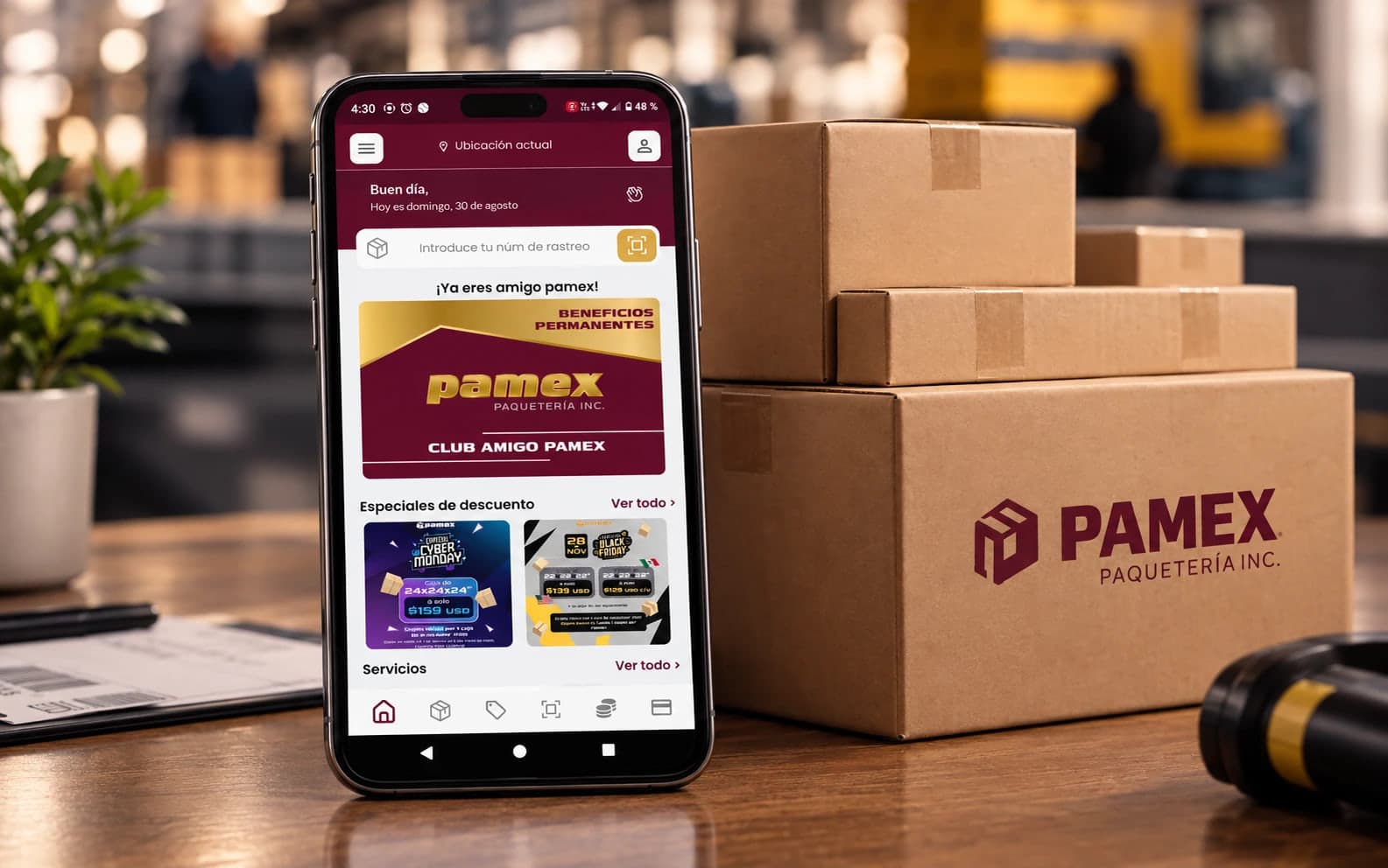 App de lealtad Club Amigo PAMEX en un teléfono, junto a cajas de paquetería